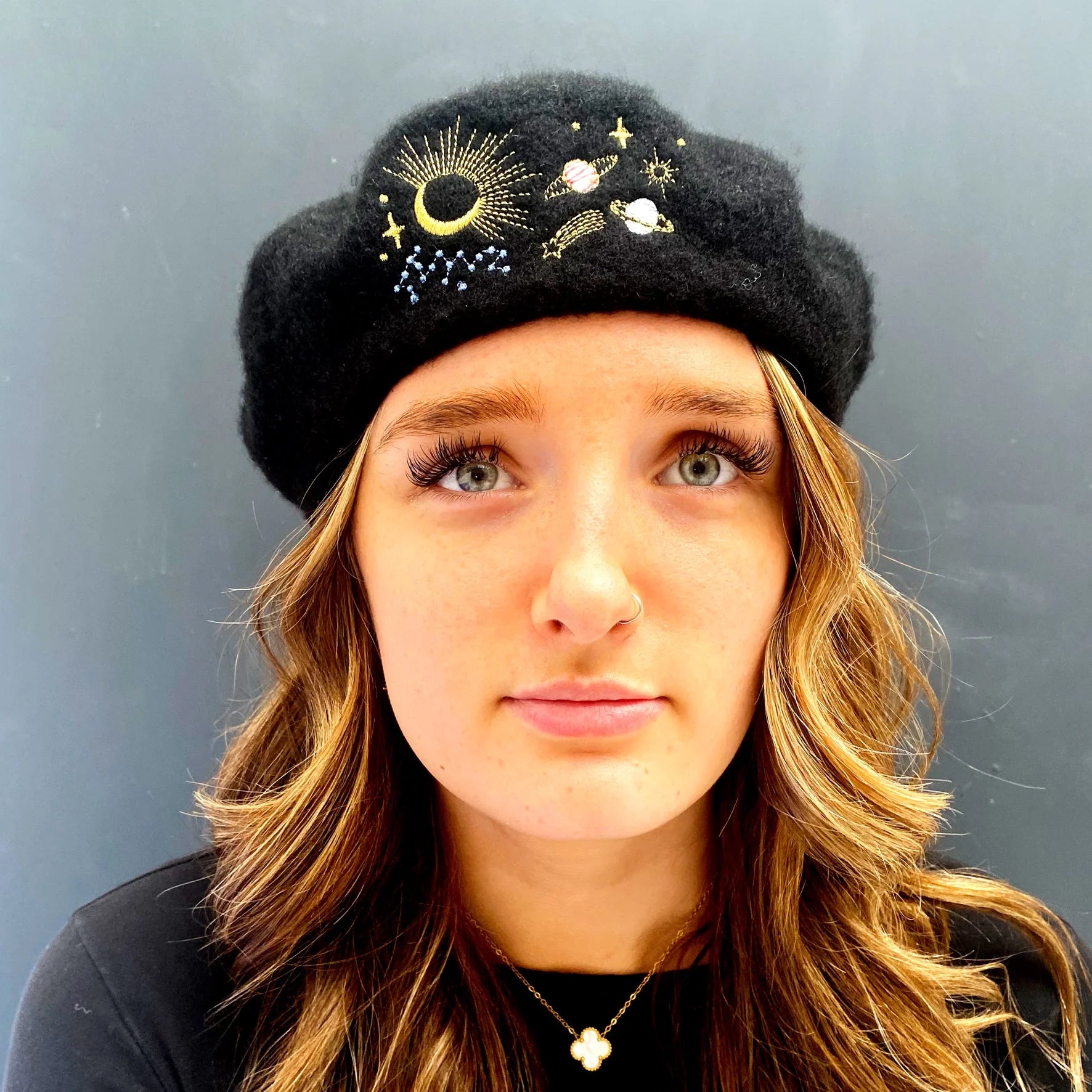 Front view of woman wearing black beret with celestial embroidery including moon, stars, and planets.