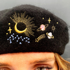 Close-up of celestial embroidery featuring moon, stars, planets, and comet on black beret.