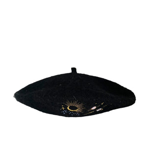 Side view of black embroidered beret with moon and planet details against white background.