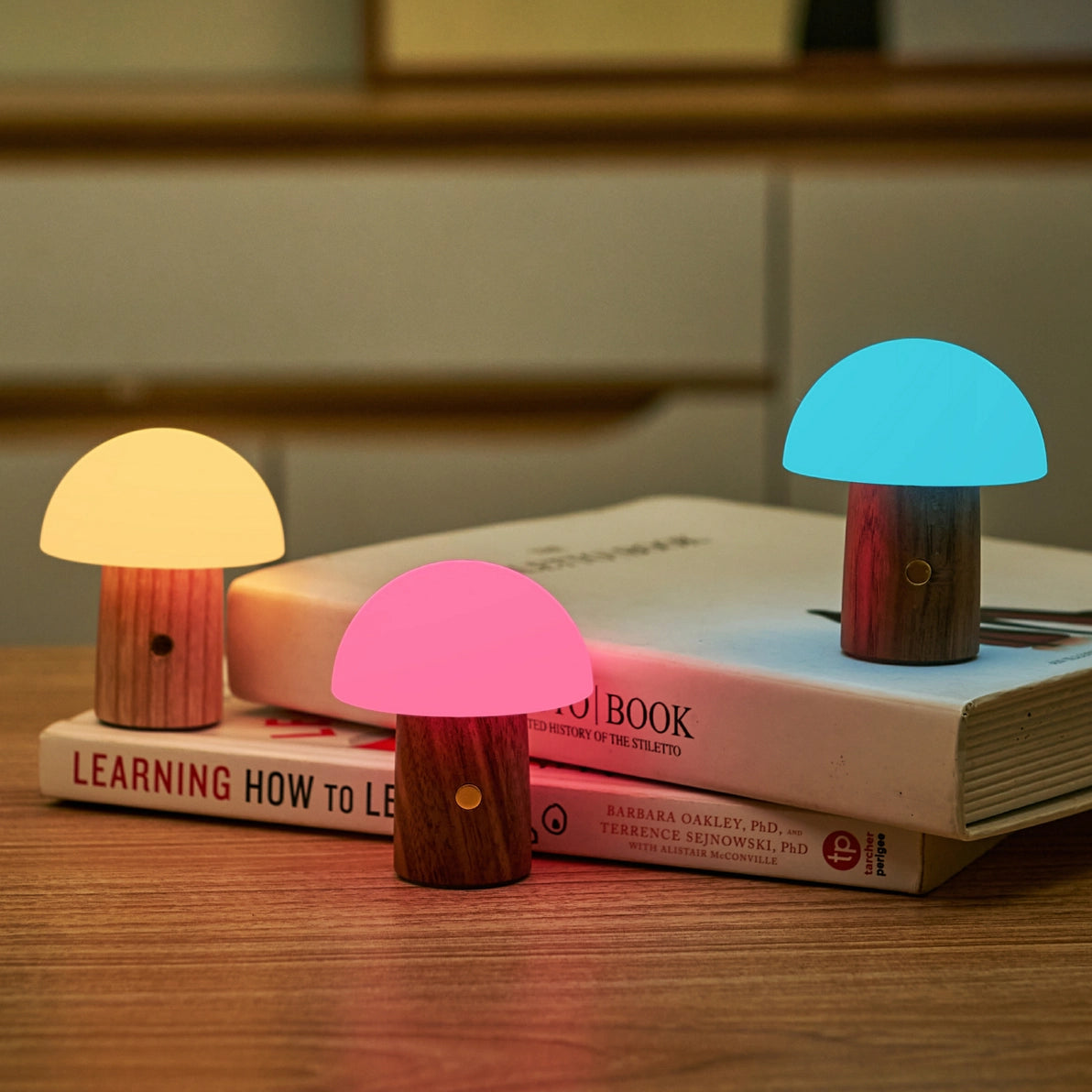 Alice Mushroom Lamp Super Mini glowing in yellow, pink, and blue on a wooden desk.