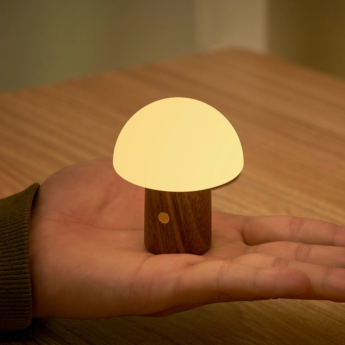 Warm white Alice Mushroom Lamp Super Mini glowing in hand on wooden table.