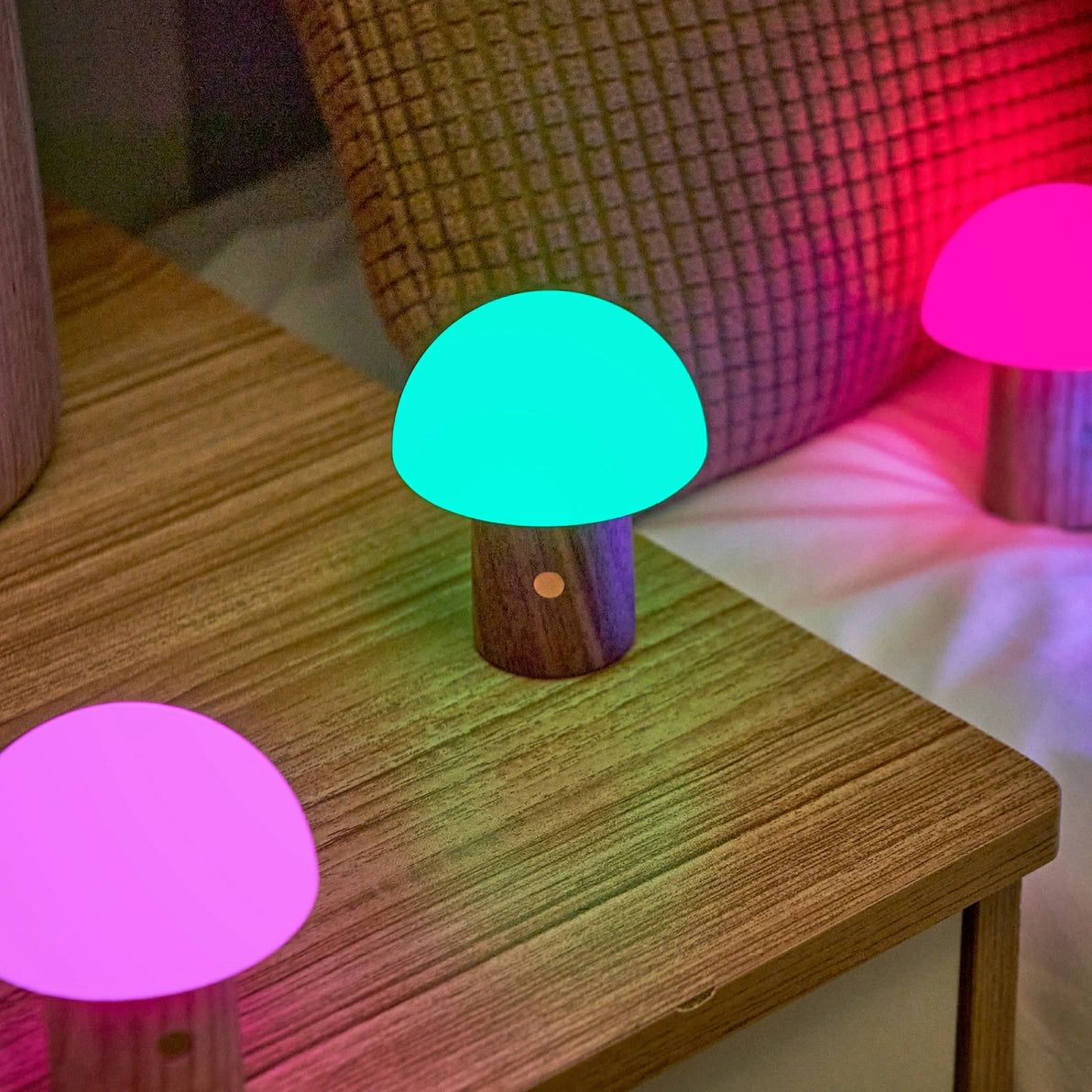 Green glowing Alice Mushroom Lamp Super Mini on wooden table beside pink lamps.