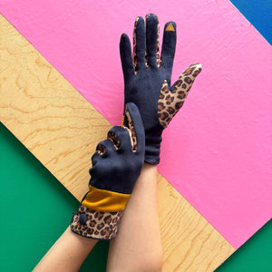 Navy leopard print gloves with touchscreen fingertip detail, shown on hands against colourful backdrop.