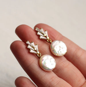 Close-up of a hand holding the Art Deco crystal pearl earrings, showcasing their intricate gold-plated setting, sparkling crystals, and lustrous freshwater pearls.