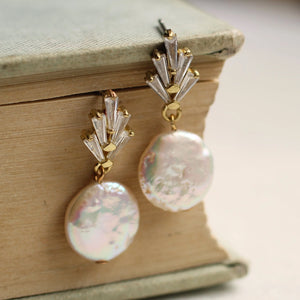 The Art Deco crystal pearl earrings displayed on the edge of an antique book, highlighting their vintage-inspired design and shimmering pearl accents.