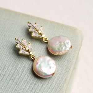 A pair of Art Deco crystal pearl earrings laid on soft fabric, emphasizing their delicate craftsmanship, sparkling baguette-cut crystals, and unique pearl sheen.