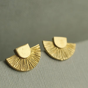 A detailed view of the gold Art Deco stud earrings placed on a fabric surface, showing their semi-circular shape and vintage-inspired brass finish.