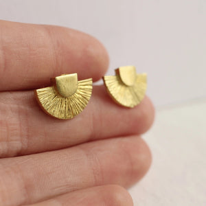 A close-up of a hand holding the gold Art Deco stud earrings, highlighting their small size and intricate sunburst texture.