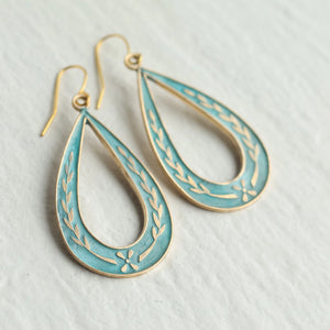 Close-up of Art Nouveau-style brass and blue enamel teardrop earrings featuring floral detailing, laid flat on white surface.