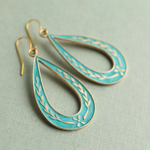 Pair of vintage-inspired brass hoop earrings with cornflower blue enamel and floral sprig motif, photographed at an angle on a soft green background.
