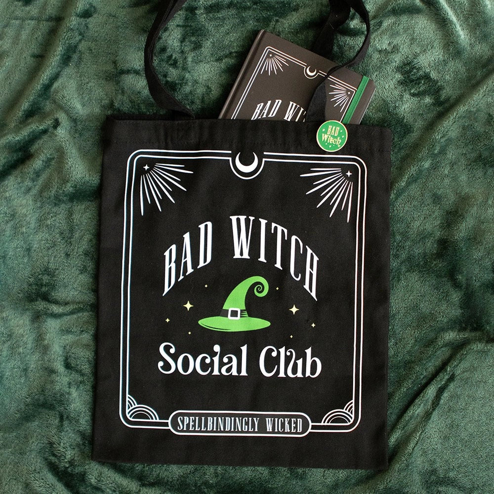 Black tote bag with “Bad Witch Social Club” design and matching pin badge on green fabric.