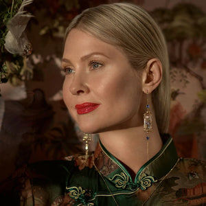 Elegant gold bird cage earrings worn by model in rich floral outfit, captured in warm lighting to highlight the enamel bird and crystal accents.
