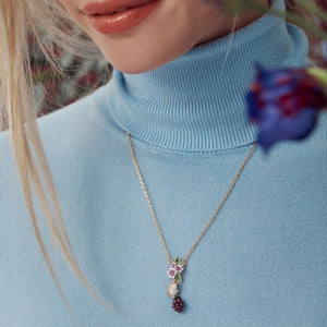 Woman wearing the Bill Skinner Blackberry & Mouse Necklace, styled over a pastel blue turtleneck, highlighting the detailed enamel charm against the neckline.
