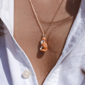 Close-up of the hand-enamelled fox pendant resting on a model’s neckline, highlighting intricate details and vibrant colour.