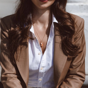 Fox necklace worn by a model seated outdoors in a brown blazer and open white shirt, styled in natural light.