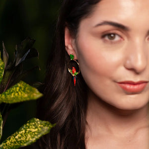 Close-up of model wearing vibrant red parrot hoop earrings by Bill Skinner, featuring gold-plated hoops, green enamel leaf studs, and tropical detailing.