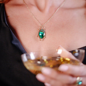 Model wearing green bug necklace in satin eveningwear holding a cocktail glass.