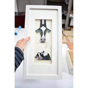 A person holding the “Rise and Shine” framed print, showing the size and detailing of the artwork, which features a Friesian cow and her sleepy calf.