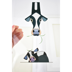 A close-up of the transparent acrylic glass print from “Rise and Shine,” featuring a Friesian cow and her calf, held up to reveal its delicate shadow effect.