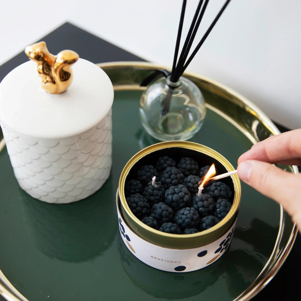 Close-up of hand lighting Cinnamon Blackberry CandleCan on decorative tray, showing luxury home styling and candle in use.