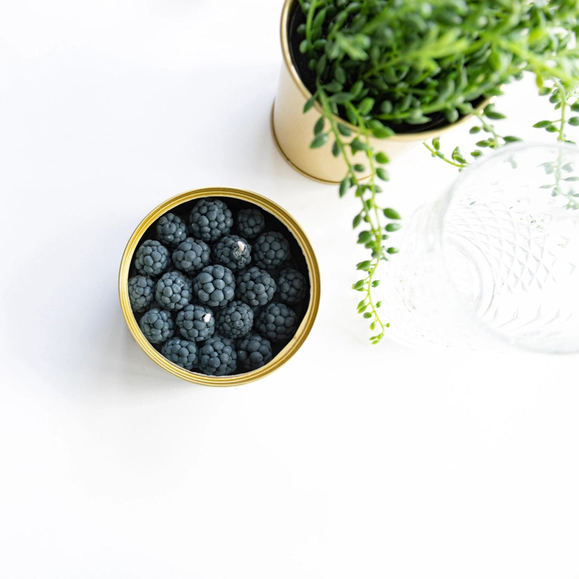 Blackberry CandleCan styled with greenery on white tabletop, highlighting realistic fruit-like design and artisan detail.