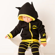 Baby sitting on white chair in Batman “Get Ready” Hoodie with yellow trim and matching black-and-yellow striped Batman leggings.