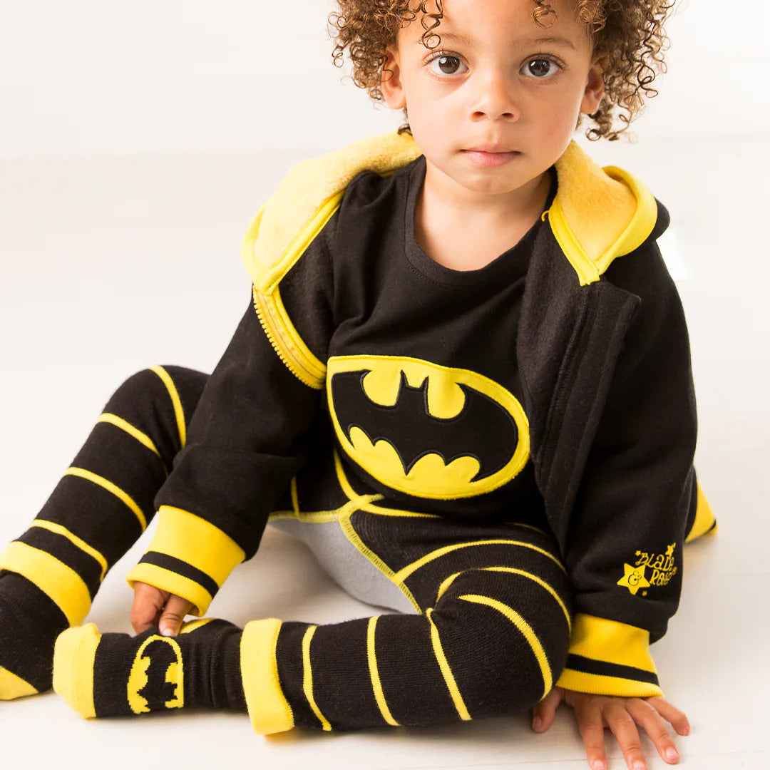 Toddler sitting on floor in full Batman “Get Ready” outfit including hoodie, bat logo t-shirt, striped leggings, and Batman socks.