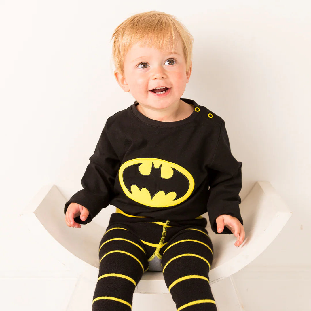 Toddler wearing Batman™ “Get Ready” Top with yellow logo and striped leggings.