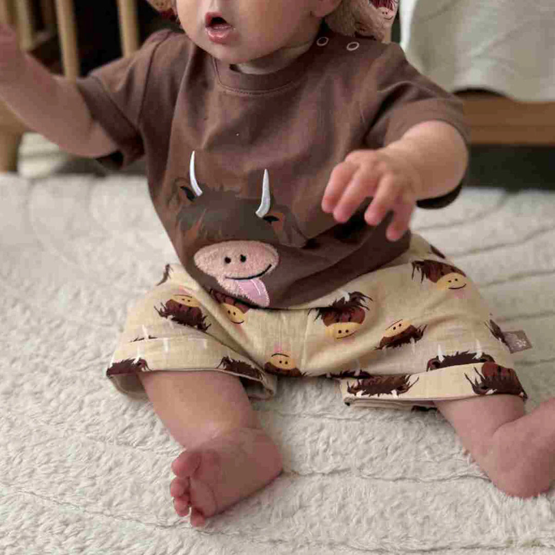 Baby wearing cream cotton shorts with highland cow print