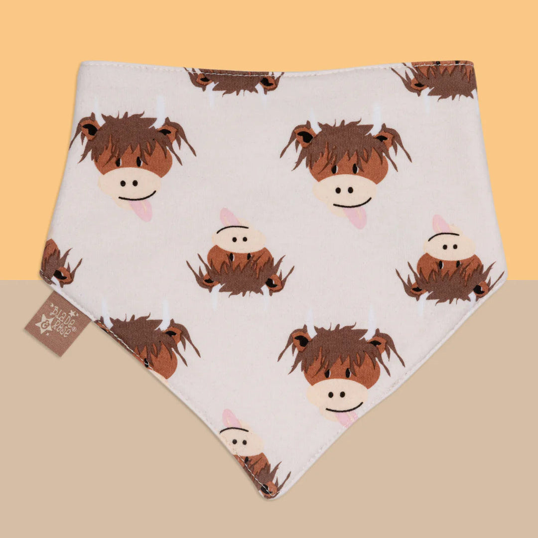 Flat lay of neutral Hamish Highland Cow bib with all-over smiling cow face print in brown and off-white, featuring Blade & Rose logo tag.