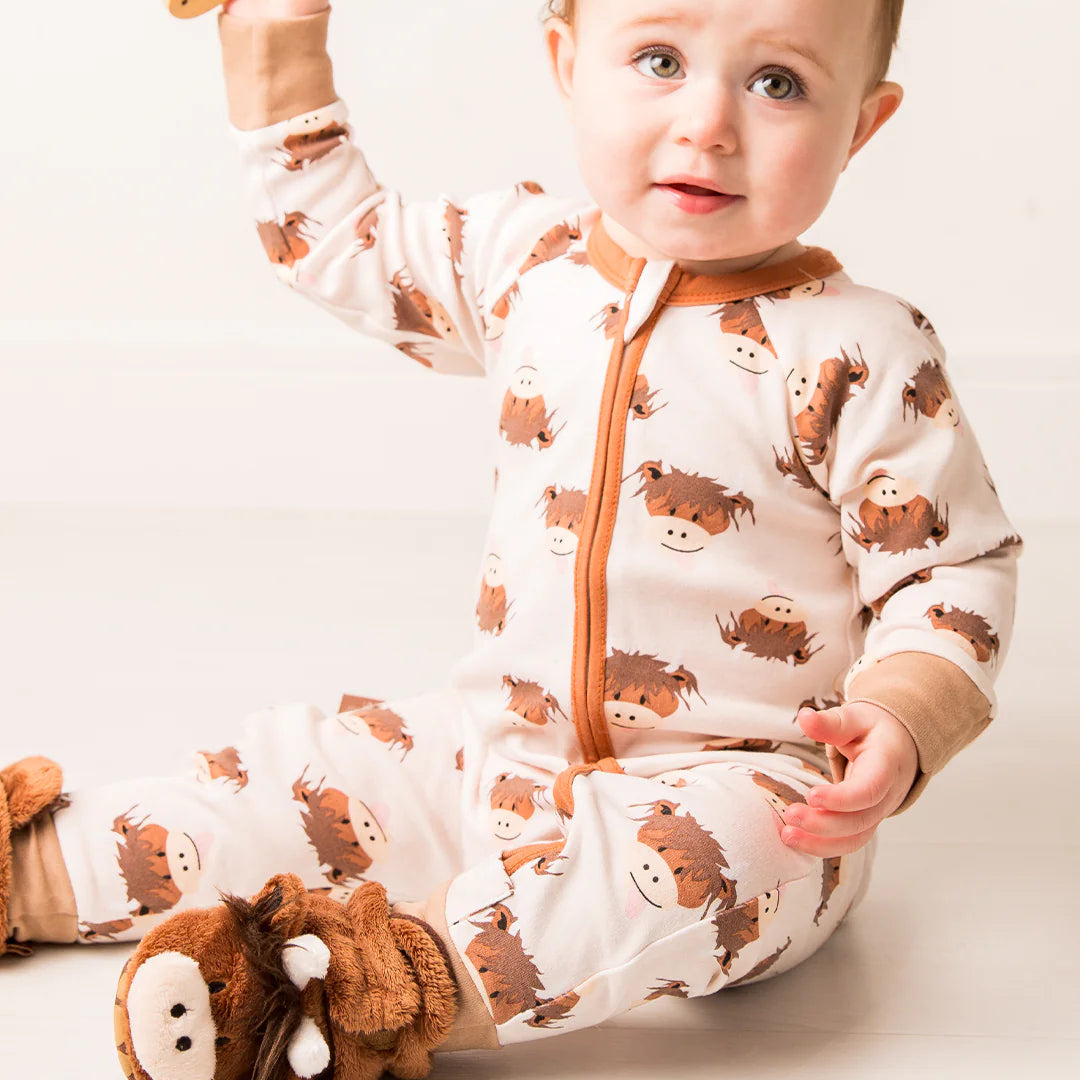 Baby wearing a Neutral Highland Cow romper holding a toy, showcasing the all-over cow face print and cosy fit.