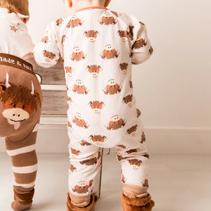 Back view of baby standing in Neutral Highland Cow romper, showing the full cow print and contrast neckline.