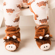 Baby wearing Neutral Highland Cow Booties with romper – soft brown cow face slippers on white floor.