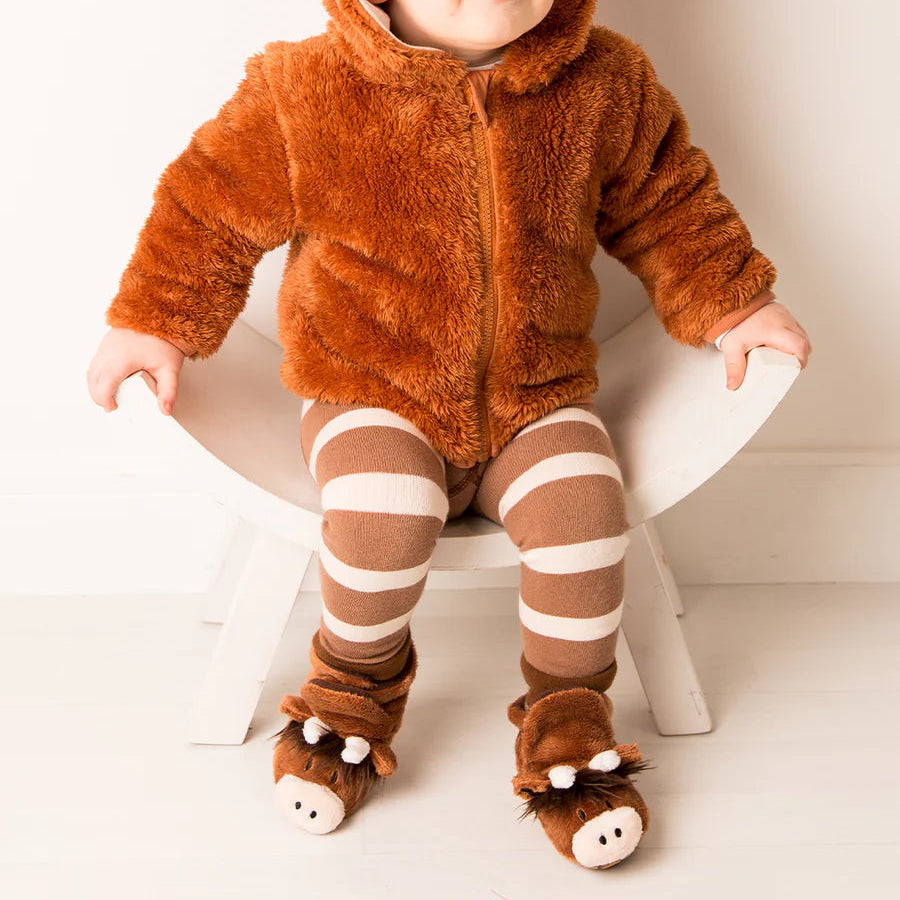 Toddler in Highland Cow outfit and booties, seated in chair wearing fuzzy brown cow hoodie and striped leggings.