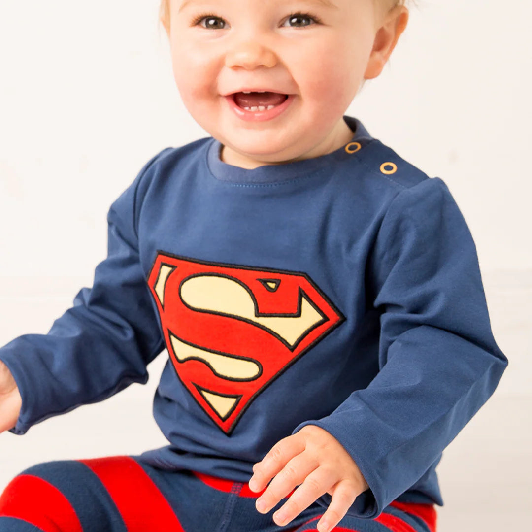 Smiling baby in Superman™ blue top and matching red and blue striped leggings.