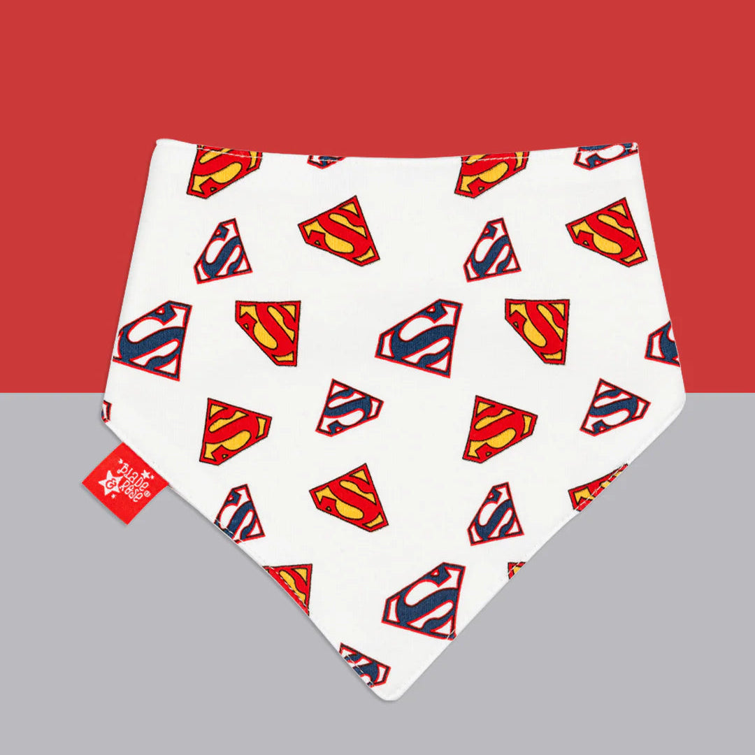 White Superman™ baby bib with repeated red and yellow “S” shield logos, displayed flat on a red and grey background.