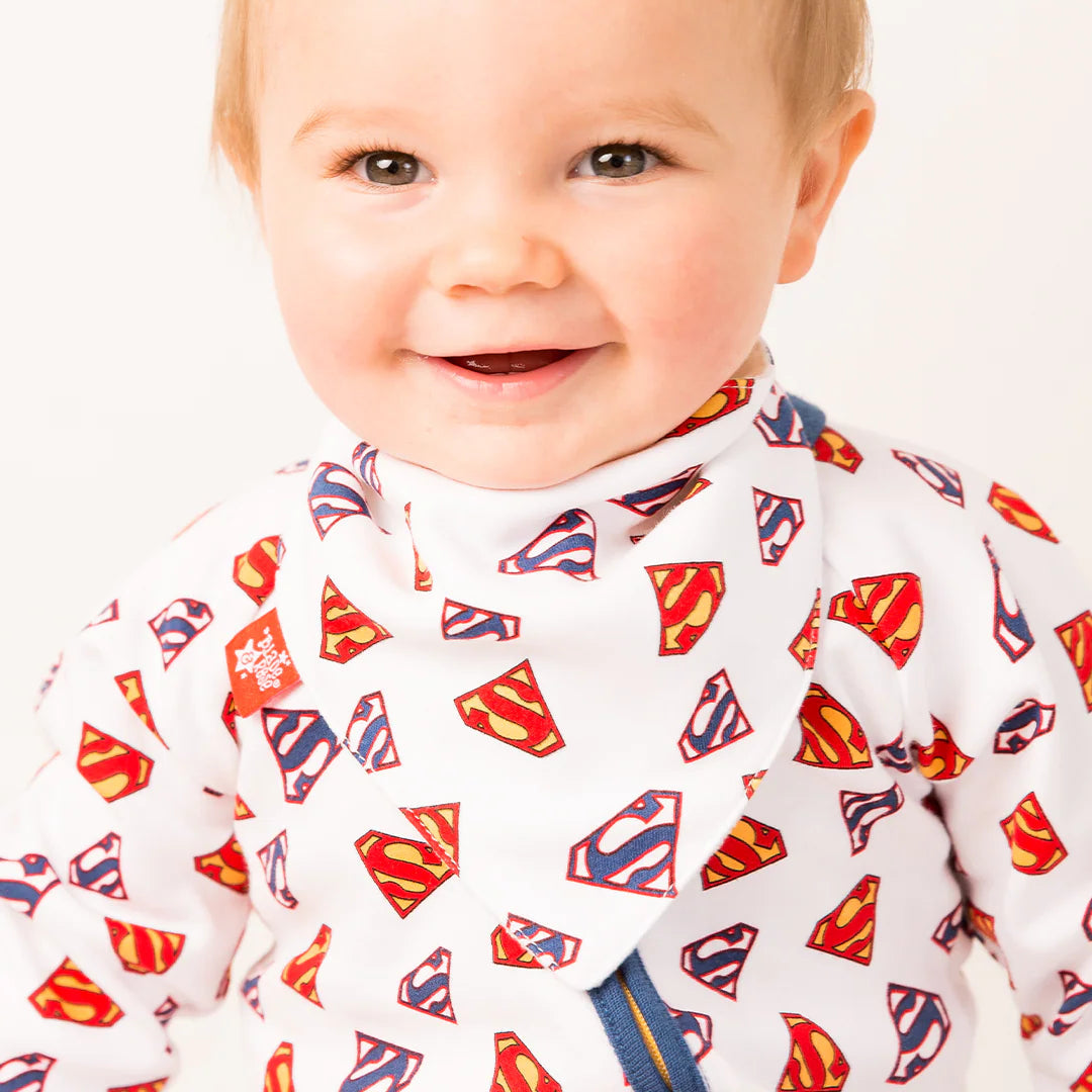 Smiling baby wearing white Superman™ bib with all-over logo print, matching logo print outfit.