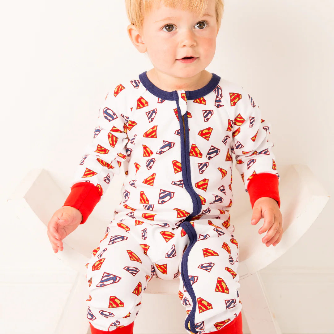 Baby sitting in Superman Save The Day Zip Up Romper featuring white fabric with all-over Superman shield print, red cuffs, and navy zip front.