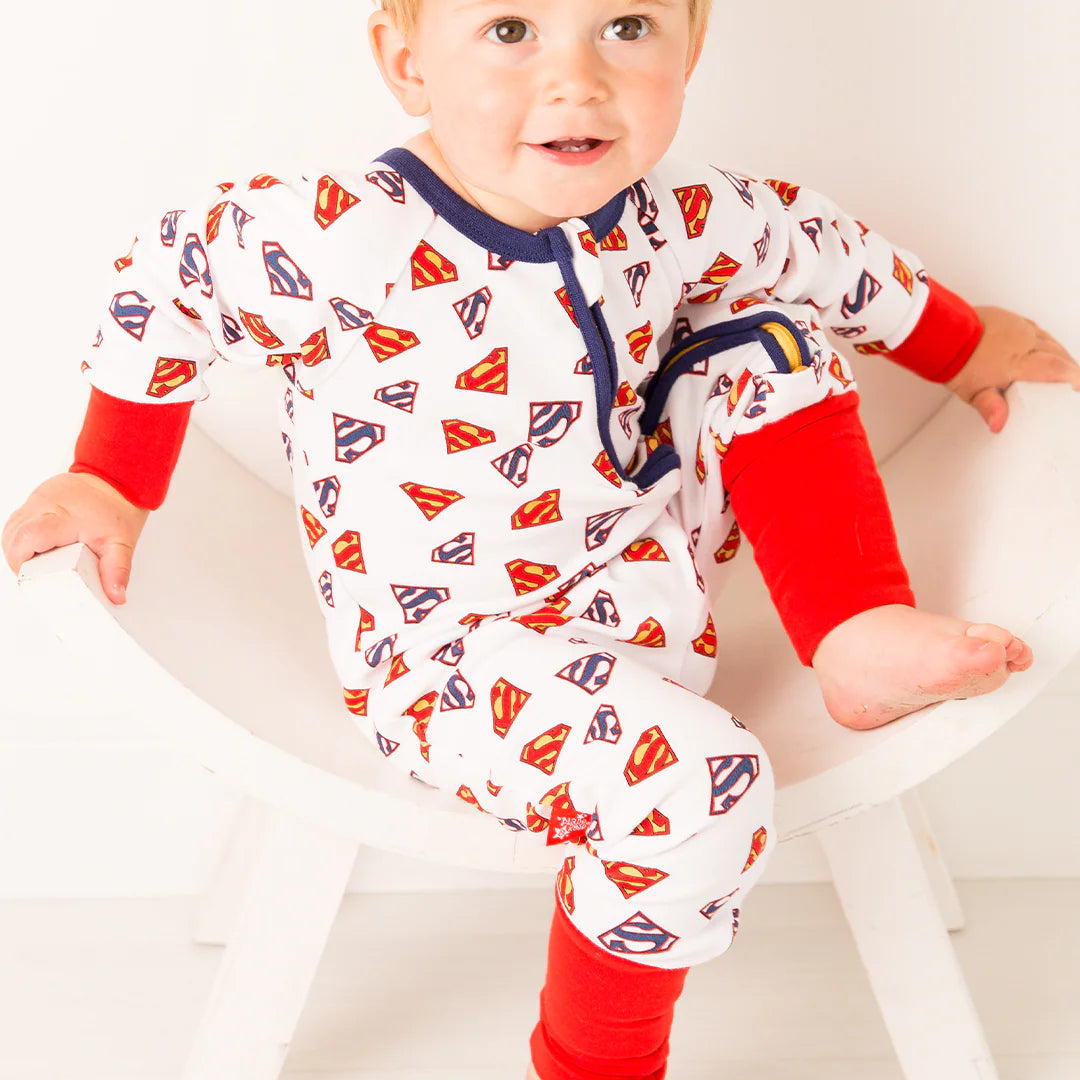 Baby seated sideways in Superman Save The Day Zip Up Romper with foldable red cuffs, white cotton base, and vibrant Superman shield print.
