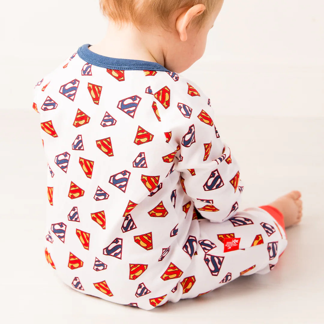 Back view of baby wearing Superman Save The Day Zip Up Romper showing all-over red and yellow Superman shield print on white cotton fabric with red cuffs.