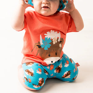 Toddler in matching Bonnie Highland Cow outfit with orange tee and printed hat.