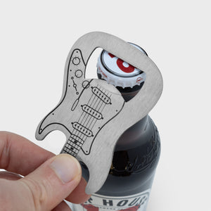Close-up of hand using stainless steel electric guitar bottle opener to remove the cap from a brown glass beer bottle.