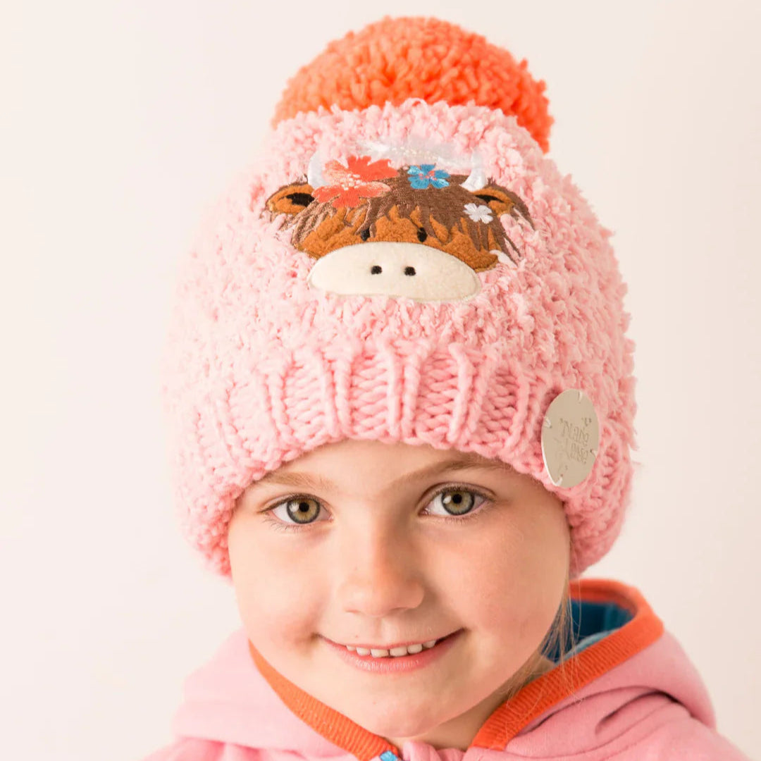 Child wearing Bonnie Highland Cow Winter Hat – pink knit with cow motif and pom pom.