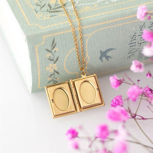 Open view of the gold book locket necklace showing two oval photo slots inside.