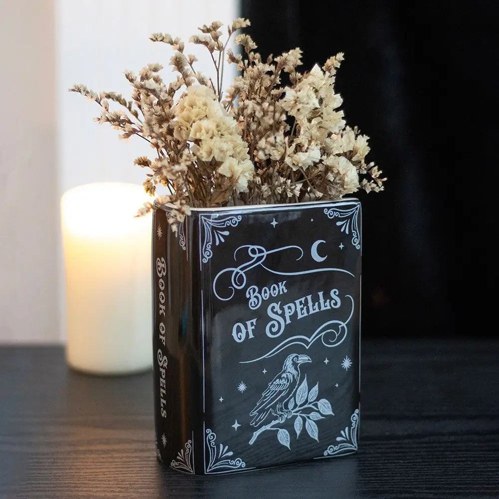 Book of Spells vase styled with dried flowers and candle. Ceramic Book of Spells gothic vase with dried flowers, styled on dark wood with glowing candle in background for moody home décor.