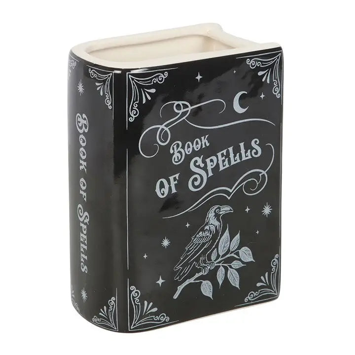 Angled front view of ceramic spellbook vase. Black and white ceramic flower vase shaped like a spellbook with ‘Book of Spells’ text and raven illustration on front.