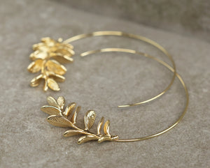 Gold botanical hoop earrings displayed on a textured background, highlighting the intricate leaf detailing.