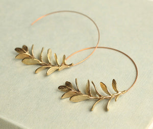 A pair of brass botanical leaf hoop earrings resting on a jewellery box, showing their rich golden finish.