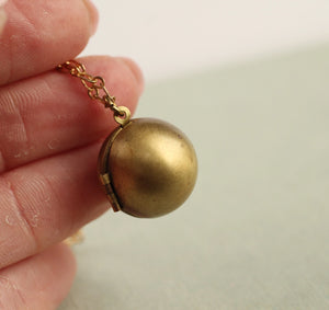 A hand holding the brass sphere locket necklace, highlighting its size and beautifully aged patina.