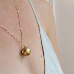  The brass sphere locket necklace worn by a model, draping elegantly from an 18-inch chain, complementing a minimalist outfit.
